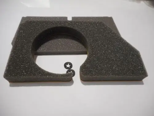 Remeha Isolierung für einen Luftkasten, gefertigt aus grauem Schaumstoff mit abgerundeten Kanten. Zwei schwarze Kunststoffscheiben liegen daneben.